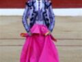 Un torero en traje tradicional, con un chaleco azul y blanco, camisa blanca y falda rosa brillante.