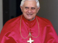 Imponente imagen del Papa Benedicto XVI en su vestimenta papal roja, con una sonrisa y una cruz de oro al cuello.