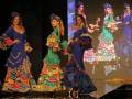 Desfile de moda flamenca con modelos en trajes coloridos y volantes en un escenario iluminado.