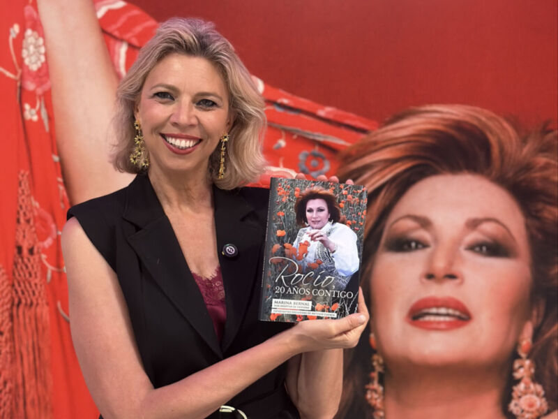 Una mujer sonríe mientras sostiene un libro titulado 'Rocio: 20 años contigo' en una presentación.