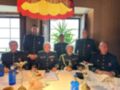 Un grupo de personas en uniforme militar se reúnen a la mesa para una reunión formal. La imagen muestra a siete individuos sentados en una mesa, con un ambiente formal y decorado con flores y botellas de agua. La escena transmite una sensación de respeto y solemnidad, típica de un evento oficial o ceremonial.