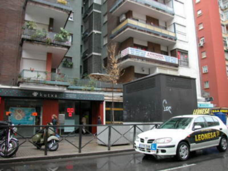 Vista de una calle con edificios de varios pisos, una motocicleta aparcada y un coche blanco con la inscripción 'LEONESA' en el lateral.