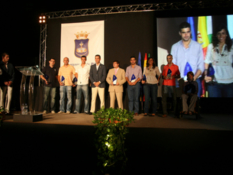 Una ceremonia de premiación en un escenario con una pantalla proyectando imágenes de personas.