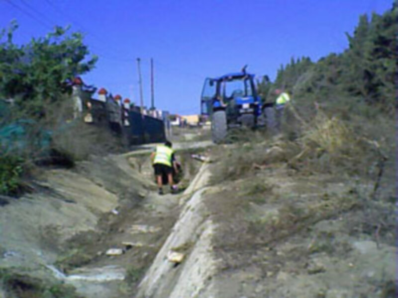 Trabajadores en una obra de construcción en una pendiente, con un tractor en el fondo y un canal de agua en el suelo.