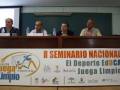 En el II Seminario Nacional "El Deporte EduCA Juega Limpio", se presentan cuatro oradores sentados detrás de una mesa con un cartel informativo en la UCA.