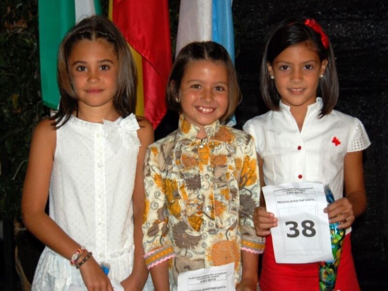 Tres niñas sonrientes posan con banderas y un cartel número 38.