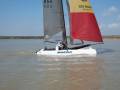 Barco de vela Nacra navegando en el agua con el número 854 en el asta y el nombre 'GIS GROUP Romania' en la popa.