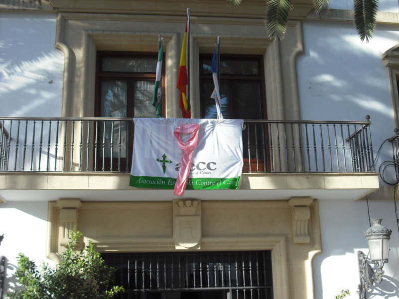 Balcony of a building with flags and a banner promoting 'AECC' (Asociación Española Contra el Cáncer).