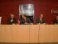 Presentación en Fundación Cruzcampo, tres hombres en trajes sentados detrás de una mesa con micrófonos.