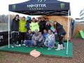 Gruppo de personas posando en un área al aire libre con una tienda Monster Energy.