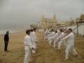 Entrenamiento de artes marciales en la playa con un escenario histórico al fondo.