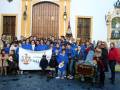 Grupo de personas con uniforme azul y bandera de 'Hermanos del Museo', posando frente a una fachada histórica decorada con motivos navideños.