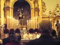 Una procesión religiosa en una iglesia con velas encendidas y un altar dorado.