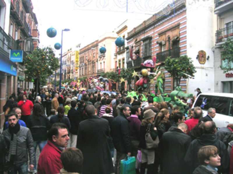 Fiesta en una calle con globos, carros y personas celebrando.