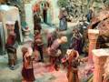 Escena navideña con figuras de personas en una representación de la Natividad. Personajes vestidos con trajes medievales y un arco en el fondo, posiblemente representando la entrada al Santuario.