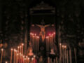 Una imagen de un altar con velas encendidas y una figura en la cruz, iluminada por el rojo de las velas.