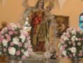 Estatua de la Virgen con el Niño Jesús, adornada con flores y ornamentos en un altar religioso.