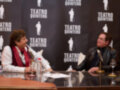 Dos hombres se sientan en una mesa con microfonos y copas de vino, frente a un fondo negro con el texto "Teatro Quintero".