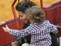 Una madre sostiene a su hijo en brazos, ambos sonríen y parecen disfrutar de la experiencia. La imagen se centra en el momento de felicidad y conexión entre madre e hijo, capturando un instante inolvidable.