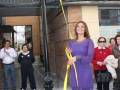 Una mujer en un vestido púrpura corto corta una cinta amarilla para inauguración de Plaza María José Suárez.