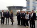 Un grupo de personas en trajes posa frente a un edificio moderno con una estructura curva, probablemente en un evento oficial o de inauguración.