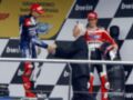 Un piloto de motocicleta celebra con un juez en el podio, mientras otro piloto observa. La bandera de Ducati y el escudo de la FIM están visibles en el fondo.