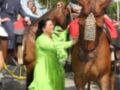 Una mujer en un vestido verde brillante sostiene la correa de un caballo mientras otros participantes, incluyendo una niña y un hombre en traje, observan.