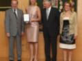 Premio entregado en una ceremonia formal, con una mujer recibiendo un reconocimiento de manos de autoridades.