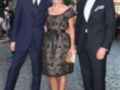 Una familia elegante posa en un evento formal. La madre, vestida con un vestido negro de encaje, sostiene una cartera. El padre, también en traje negro, mira hacia la cámara con orgullo. El hijo, con una camisa blanca y corbata negra, sonríe ampliamente. La escena transmite un ambiente de celebración y elegancia.
