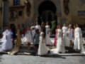Una multitud de novias vestidas con elegantes vestidos blancos posan frente a una iglesia histórica. La imagen captura la diversidad de estilos y tamaños entre las novias, con algunos vestidos más largos que otros. La arquitectura de la iglesia y el entorno urbano en el fondo completan la escena.