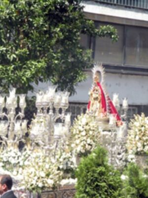 Una procesión religiosa con una imagen de la Virgen rodeada por flores y luces.