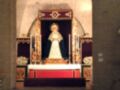 Interior de una iglesia con un altar central y una imagen religiosa en el fondo. La arquitectura es de estilo barroco con detalles dorados y rojos. La imagen central parece ser una Virgen María vestida de blanco con un velo negro.