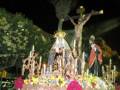 Procesión nocturna con estatuas religiosas adornadas con flores y velas.