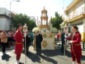 Desfile religioso con personas vestidas de rojo, un altar en el centro y edificios al fondo.