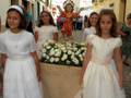 Niñas vestidas de blanco en una procesión religiosa, con un altar decorado con flores y un niño en el centro.
