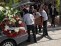 Entierro con coche fúnebre y ataúd, acompañados por personas en traje formal.