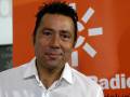 Un hombre con cabello oscuro y una sonrisa, vestido con una camisa blanca, frente a un fondo rojo con el logo de Radio Televisión.