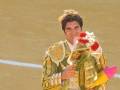 Un torero en un vestido tradicional sostiene flores y una vara de mando, posiblemente celebrando su victoria en una corrida de toros.