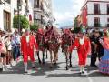 Desfile tradicional español con personajes en trajes coloridos y caballos marrones.