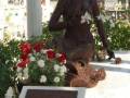 Estatua de bronce de una mujer sentada, adornada con flores blancas, en un entorno conmemorativo.