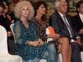Asistentes a una ceremonia formal en un ambiente con tapiz histórico en el fondo.