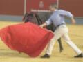 Un torero manejando un toro con un capote rojo en una plaza de toros.