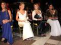 Evento de moda con modelos sentadas en sillas de madera, vestidas con elegantes vestidos de noche en un ambiente nocturno.