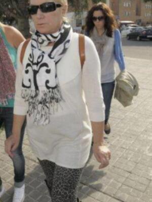 Mujer caminando por la calle con una bufanda estampada y leggings de leopardo, en un entorno urbano con otras personas y edificios al fondo.