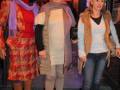 Tres personas vestidas de manera casual, con bufandas y botas. La imagen parece estar en un teatro o espacio público.