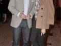 Dos personas posando en una calle, uno con chaqueta beige y pantalones vaqueros, la otra con abrigo marrón y botas.
