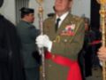 Un oficial militar en uniforme verde y rojo, con insignias y un cetro ceremonial, durante una ceremonia formal.