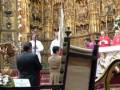 Una imagen de una ceremonia religiosa en una iglesia, con personas vestidas formalmente y un altar adornado en el fondo.