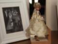 Muñeca elegante en vestido dorado junto a una foto enmarcada de una pareja en vestidos de fiesta.