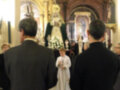 Procesión religiosa en una iglesia, con personas en trajes formales y un altar con imágenes religiosas en el fondo.